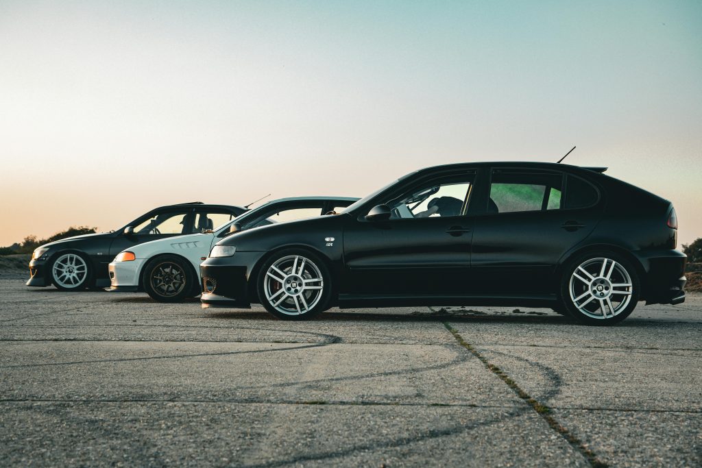 Three modern cars parked on an open road at sunset, showcasing a calm and scenic view.