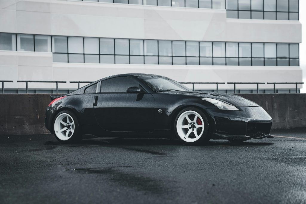 A stylish black sports car with white rims parked on a rainy day in front of a modern building.